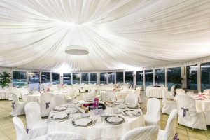white round tables with chairs around them and beautiful settings under a huge white tent
