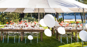 Outdoor tent setup for event with tables, chairs, flowers and balloons